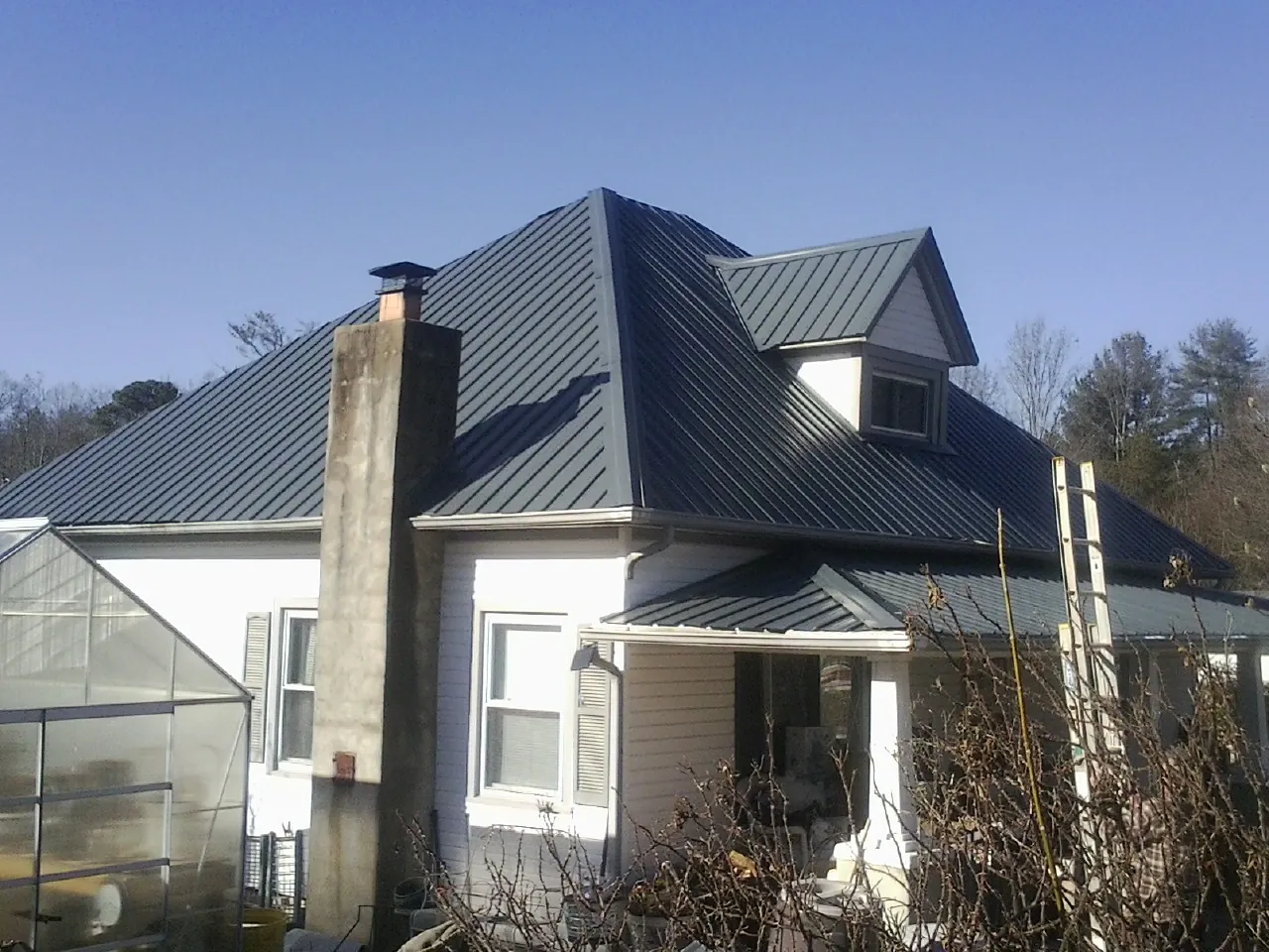 Dark blue standing seam metal roof on a white farmhouse with dormer — Slate & Tile Roof Repair by Roofing Brothers in Early Branch