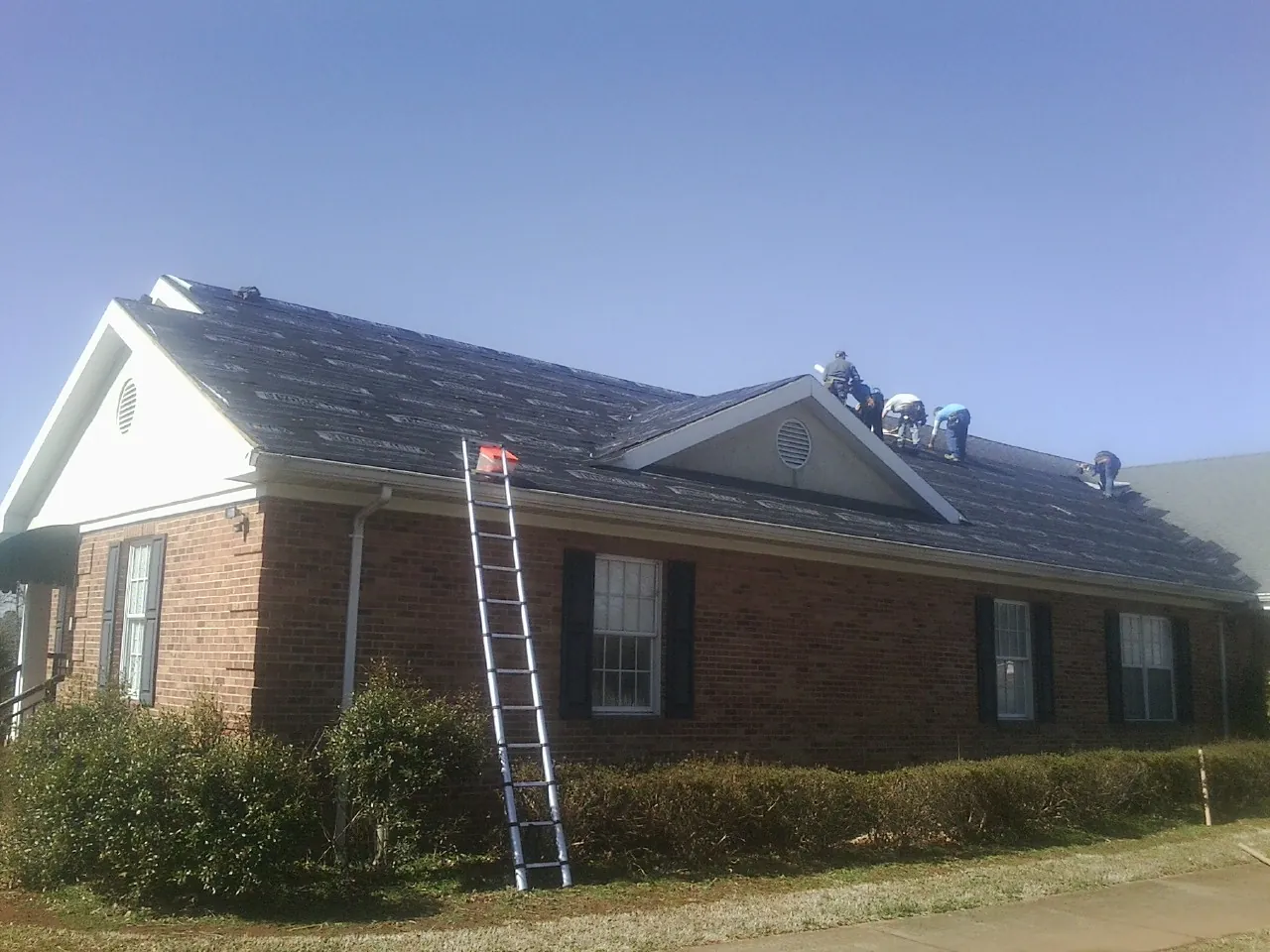 Crew tearing shingles off a brick ranch roof with a ladder set — Emergency Roof Repair work by our crew in Early Branch