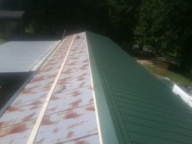 Old rusted panels beside newly installed green metal roofing — Wind Damage Roof Repair by Roofing Brothers in Early Branch
