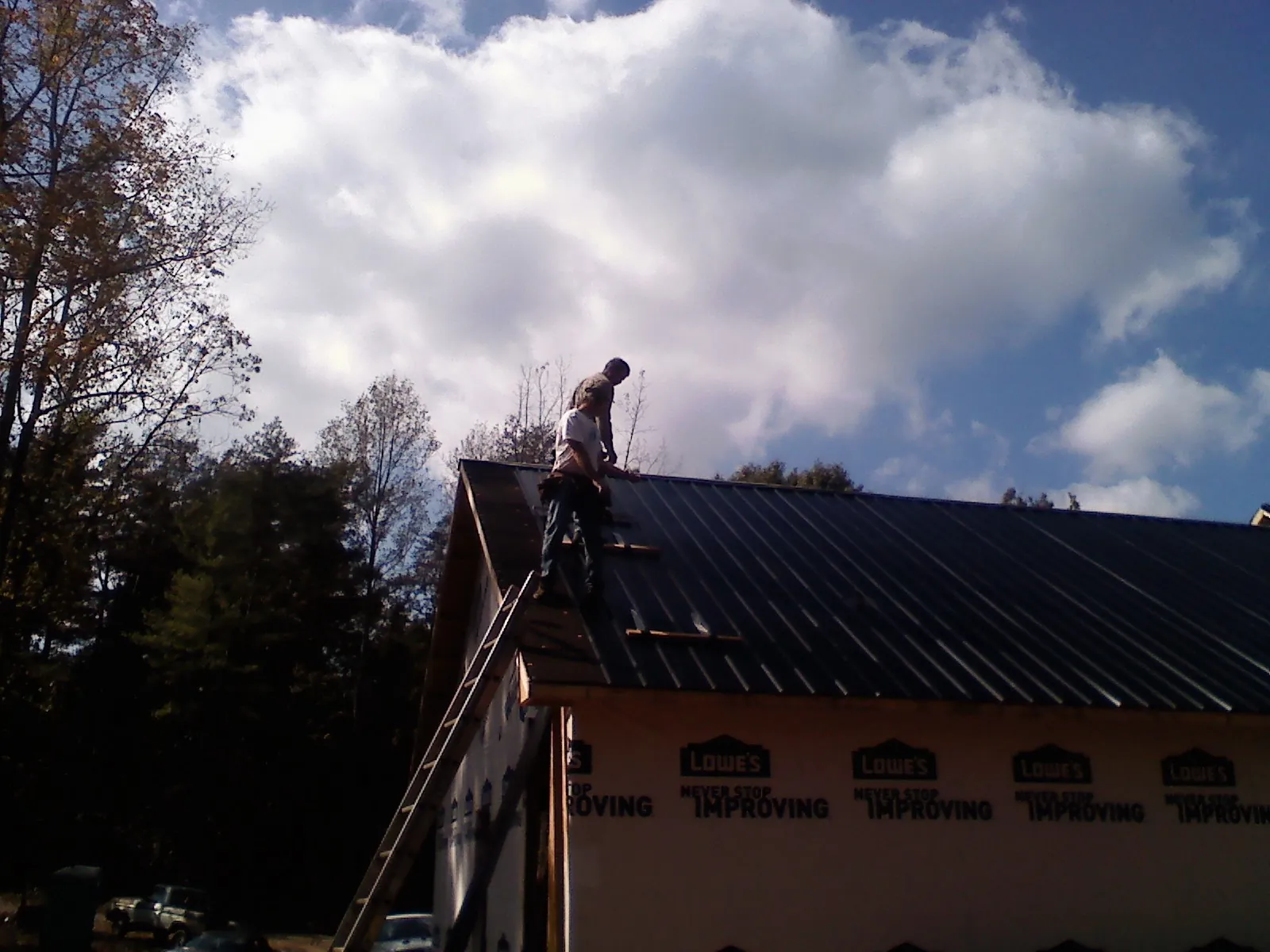 Roofer fastening dark metal panels high against a cloudy sky, from a Roof Inspection job in Early Branch