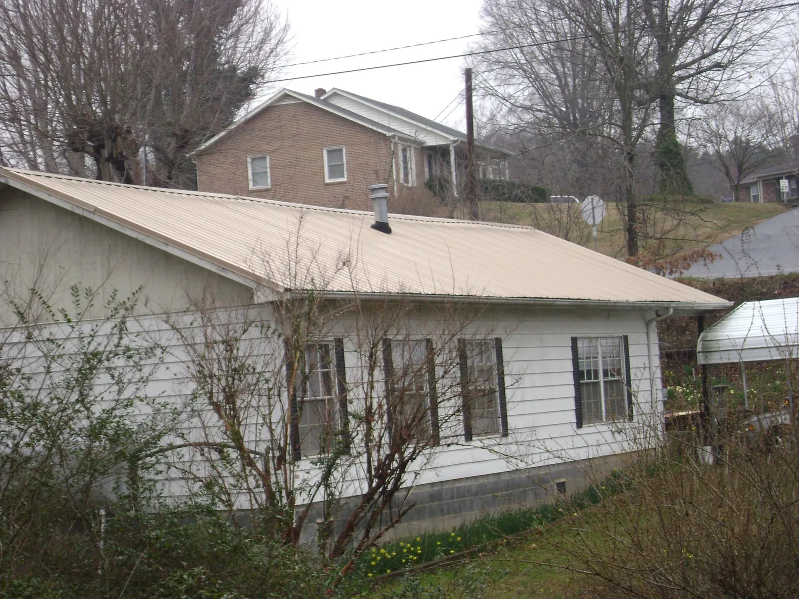 Tan metal roof on a white sided house set into a hillside — Commercial Roofing by Roofing Brothers in Early Branch